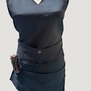 May include: Black apron with adjustable straps, multiple pockets, and a snap closure. The apron has a tool loop on the side and is designed for hairstylists.