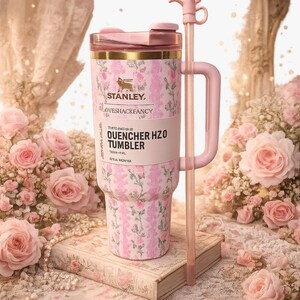 May include: A pink and white floral patterned Stanley LoveShackFancy Quencher H2O tumbler with a matching pink handle, a clear lid, and a long pink straw. The tumbler features a gold rim and the text Stanley LoveShackFancy Quencher H2O Tumbler.