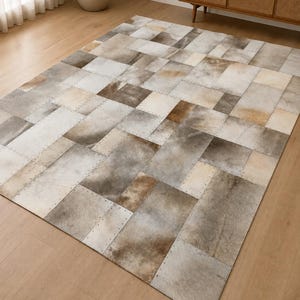 May include: A rectangular area rug composed of stitched cowhide patches in varying shades of gray, white, and brown. The individual rectangular pieces are joined together with visible stitching along the edges, creating a patchwork pattern.
