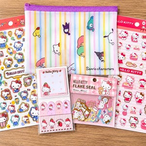Pode incluir: Um conjunto de artigos de papelaria Sanrio que inclui duas folhas grandes de autocolantes Hello Kitty, uma bolsa com fecho de correr às riscas pastel com várias personagens, um pacote de selos Hello Kitty e notas autocolantes com separadores.