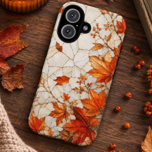 Op de afbeelding: Een rechthoekig smartphonehoesje met een witte, marmerachtige achtergrond met een gebarsten steentextuur. Het oppervlak is versierd met levendige oranje en rode herfst esdoornbladeren en kleine trosjes bessen, met een zwarte uitsparing voor de camera.