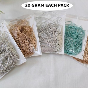 Può includere: Cinque bustine di plastica trasparente contenenti sottili cordini metallici e colorati, ciascuna etichettata 20 GRAM EACH PACK. I cordini sono avvolti all'interno delle bustine e includono i colori argento, oro, argento chiaro, verde acqua e oro rosa.