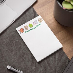 May include: A white rectangular notepad featuring the green text Nurse Katy's Notes and a row of small cartoon animals including a capybara, bear, frog, koala, and sloth, each wearing a nurse cap or holding medical equipment.