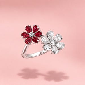 May include: A silver-toned bypass ring featuring two flower-shaped motifs. One flower is composed of five pear-cut deep red gemstones, while the other flower consists of five pear-cut clear white gemstones, both centred with a small round stone.