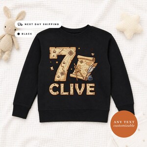 May include: A black long-sleeve sweatshirt featuring a large number seven designed with a vintage map pattern. Below the number, the name CLIVE is printed in a matching map-themed font. The graphic includes a compass, a quill, and an inkwell.