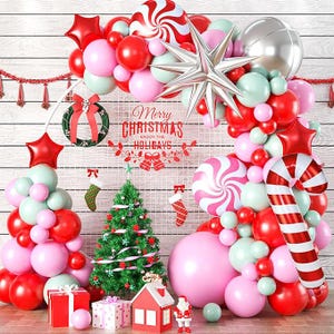 May include: A festive balloon arch featuring red, pink, and mint green balloons, a large silver star, a candy cane balloon, and a peppermint swirl balloon. A small Christmas tree, gift boxes, and a sign reading Merry Christmas Enjoy The Holidays.