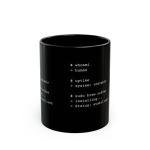 May include: A black ceramic mug featuring white monospaced text that mimics a computer terminal interface. The text reads: $ whoami > human, $ uptime > system: unstable, $ sudo brew coffee > installing..., > Status: stabilised.
