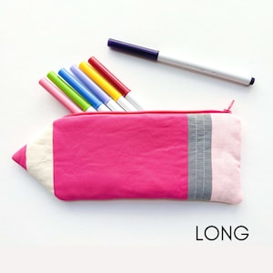K&ouml;nnte beinhalten: Eine rosa Stiftetui in Form eines Bleistifts mit einer wei&szlig;en Spitze und grauen und rosa Streifen. Das Etui liegt auf einer wei&szlig;en Oberfl&auml;che mit sieben bunten Markern, die aus der Oberseite herausragen.