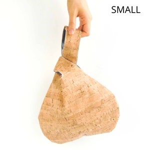 May include: A small, light brown cork handbag with a knotted handle. The bag is made of cork and has a natural, textured finish. The handle is made of cork and has a blue fabric lining.