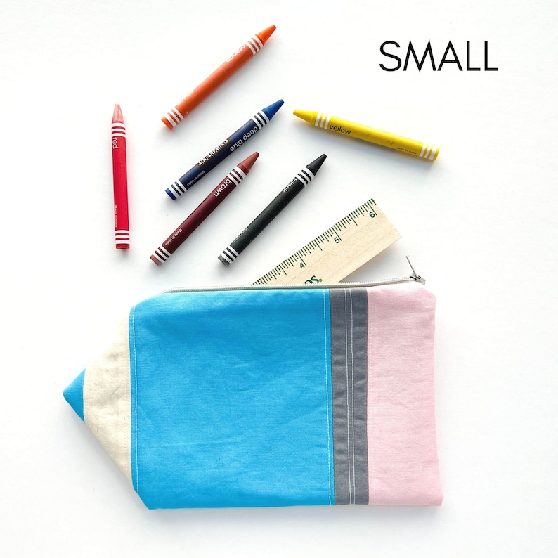K&ouml;nnte beinhalten: Eine blaue Stiftetui mit einem gestreiften Design in Pink, Grau und Wei&szlig;. Das Etui ist in Form eines Bleistifts gestaltet und hat einen Rei&szlig;verschluss. Das Etui ist von Buntstiften und einem Lineal umgeben.
