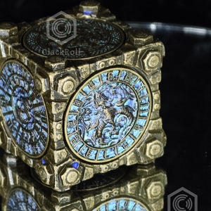 May include: A square, metallic-toned box with a weathered, antique finish. Each side features a circular, iridescent blue and purple inlay depicting a dragon-like creature surrounded by text. The box has raised, bolt-like corner details.