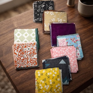 Puede incluir: Una colección de muestras de tela cuadradas con varios patrones y colores, incluyendo estampados florales en naranja, amarillo y rosa, una tela verde con patrón de estrellas, un estampado geométrico oscuro, un terciopelo morado liso y un estampado animal negro.