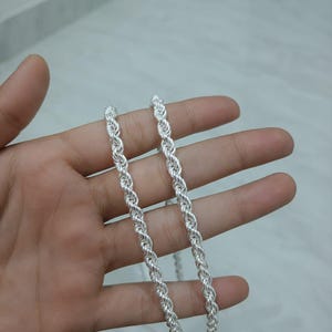 Op de afbeelding: Een glanzende zilverkleurige touwketting met een doorlopend gedraaid metalen schakelontwerp. De ketting heeft een gepolijst, reflecterend oppervlak en een gelijkmatige dikte over de gehele lengte, wat zorgt voor een eenvoudig sieraad.
