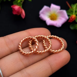 May include: Three copper rings featuring a twisted rope design. Each ring has a metallic, reddish-brown finish and a continuous circular shape. The rings are displayed together, showcasing the uniform texture and polished appearance of the metal.