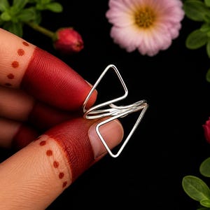 Peut inclure: Une bague en argent au design géométrique composé de deux formes triangulaires ouvertes reliées par une bande centrale. La bague est fabriquée à partir d'un fil d'argent fin et poli, créant une structure légère et ouverte entre les doigts.