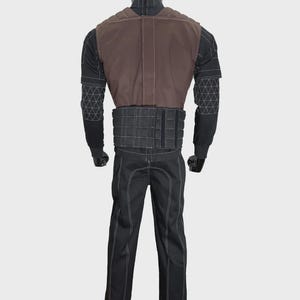 May include: A black long-sleeved shirt and pants set featuring white contrast stitching and a geometric grid pattern on the sleeves. A brown vest with padded shoulder detailing and a black quilted waist belt are worn over the shirt.