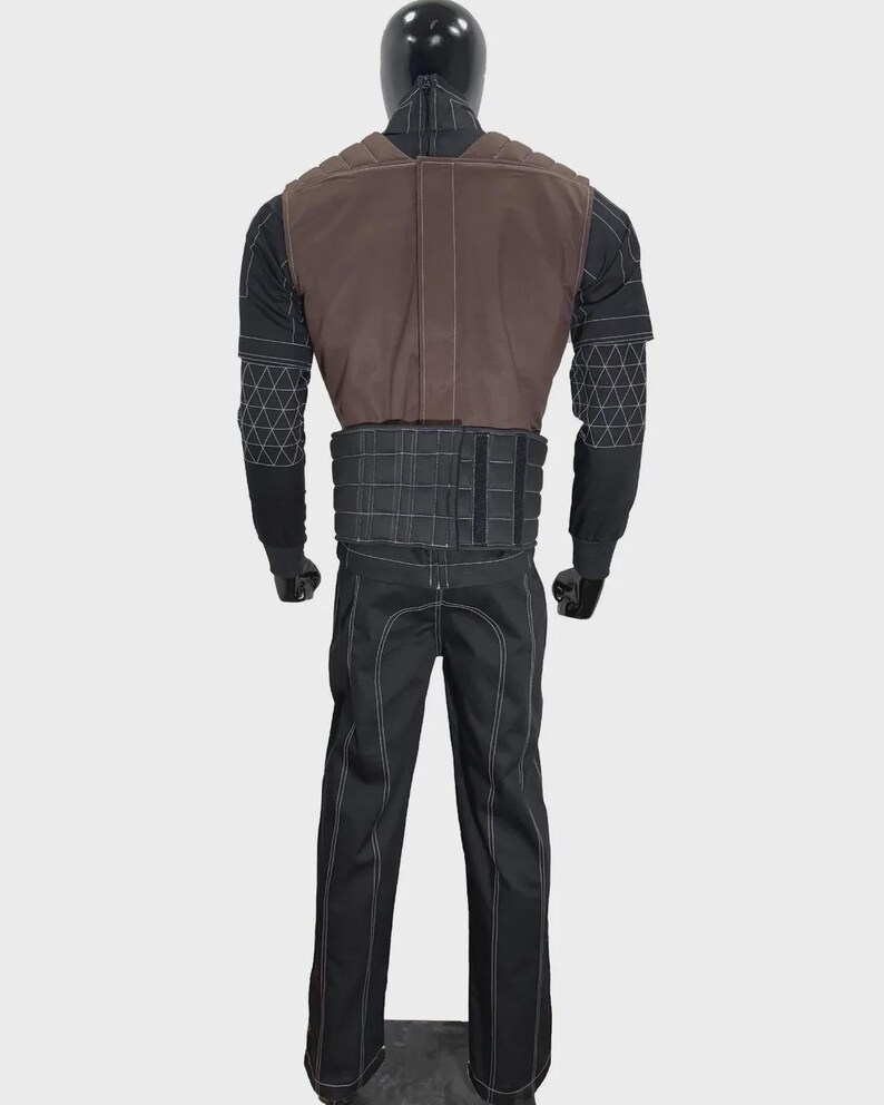 May include: A black long-sleeved shirt and pants set featuring white contrast stitching and a geometric grid pattern on the sleeves. A brown vest with padded shoulder detailing and a black quilted waist belt are worn over the shirt.