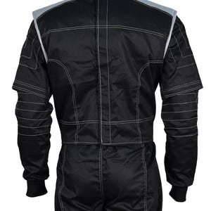 May include: A black racing suit featuring a high collar, long sleeves with ribbed cuffs, and prominent white contrast stitching throughout. The garment includes grey shoulder panels and a vertical central closure, showcasing a structured design.