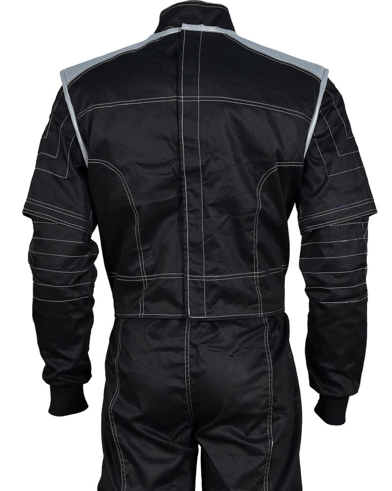 May include: A black racing suit featuring a high collar, long sleeves with ribbed cuffs, and prominent white contrast stitching throughout. The garment includes grey shoulder panels and a vertical central closure, showcasing a structured design.
