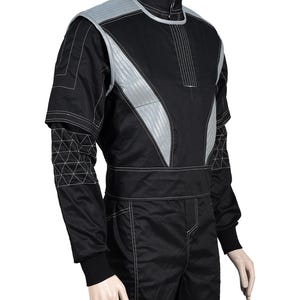 May include: A black and grey tactical-style jacket featuring a high collar, a front zipper closure, and quilted grey panels on the chest and shoulders. The sleeves include a geometric stitched pattern, and the garment has white contrast stitching.