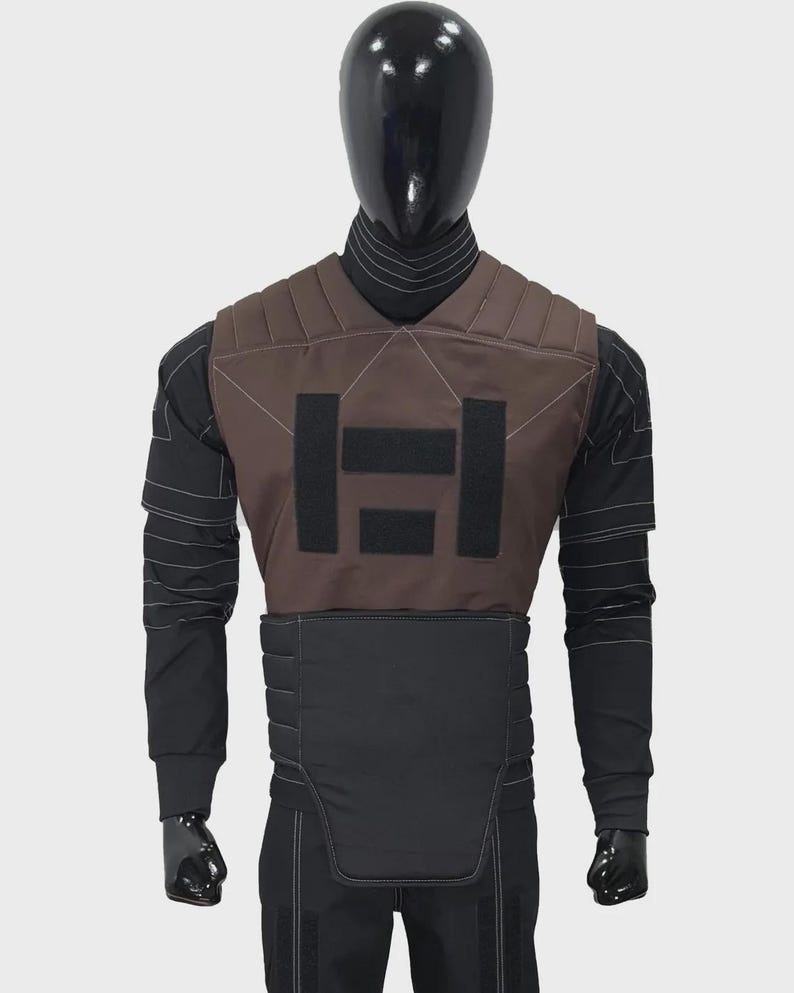 May include: A brown and black tactical vest featuring horizontal quilted padding, three rectangular black hook-and-loop fastener patches on the chest, and a high collar, worn over a black long-sleeved shirt with white decorative stitching details.