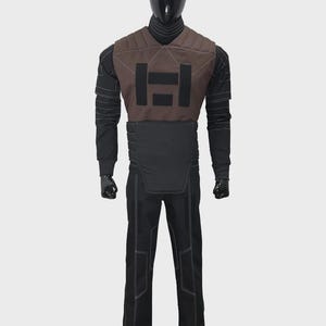 May include: A full-body costume featuring a black long-sleeved shirt with white stitching, a brown chest piece with a black rectangular graphic, and a black waist guard. The outfit includes matching black trousers with white seam detailing.