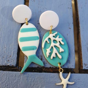 Brincos com pingentes esmaltados apresentando peixes listrados em turquesa e branco, coral branco e estrela-do-mar branca.