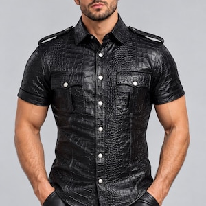 May include: A short-sleeved black shirt with a textured crocodile skin pattern. The shirt features a classic collar, two chest pockets with silver-toned snap buttons, matching silver-toned buttons down the front placket, and shoulder epaulets.