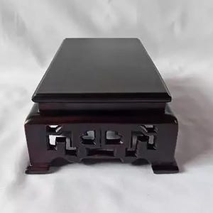 Può includere: Un espositore rettangolare in legno marrone scuro con una superficie superiore liscia e piatta e una base caratterizzata da intricati motivi geometrici intagliati a giorno. Il supporto è rialzato su quattro piedi corti e robusti.