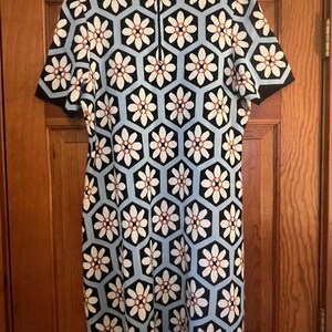 May include: A short-sleeved dress featuring a geometric floral pattern. The dress has a black, white, and light blue color scheme. The flowers are white with a brown center, set within black and light blue hexagons.