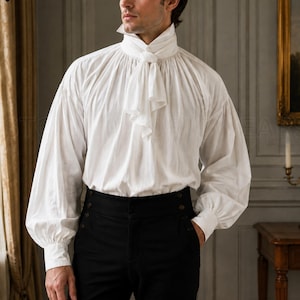 May include: A white long-sleeved shirt with a high collar and a tied neck scarf, paired with black high-waisted trousers featuring side buttons. The shirt has full, gathered sleeves and a loose fit, while the trousers have a structured waistband.