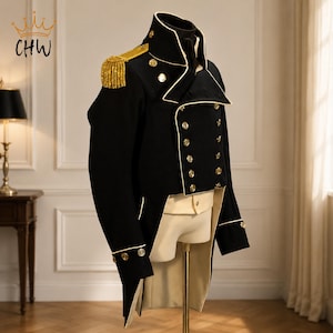 May include: A black military-style tailcoat featuring gold-toned buttons, white piping along the lapels and cuffs, and a gold fringed epaulet on the shoulder. The jacket is displayed on a mannequin, revealing a cream-coloured vest underneath.
