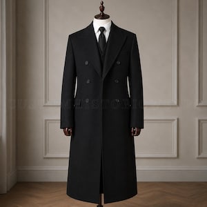 May include: A black double-breasted long coat featuring a wide lapel, six front buttons, and two flap pockets. The coat is worn over a white collared shirt and a black necktie, displayed on a mannequin torso against a paneled wall background.