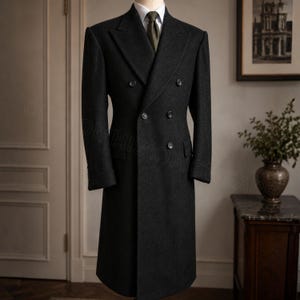 Puede incluir: Un abrigo cruzado de lana gris carbón con cuello estructurado, solapas anchas y seis botones oscuros. El abrigo se lleva sobre una camisa blanca de cuello rígido y una corbata de color verde oliva oscuro, creando una silueta formal.
