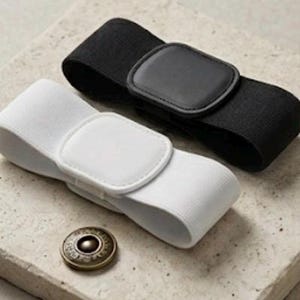 以下が含まれることがあります： 黒と白の伸縮性のあるベルトが2本。それぞれ角が丸い長方形のバックルが付いています。ベルトの近くの質感のある表面には、模様が刻印された円形の金属製ボタンが1つ置かれています。