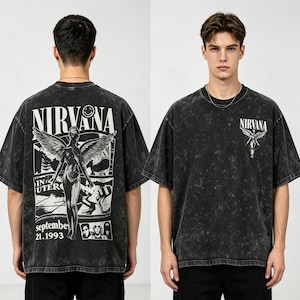 May include: A black acid-wash t-shirt featuring a graphic print. The back displays a large winged figure, the text NIRVANA, a smiley face, and the date September 21, 1993. The front features a smaller graphic of a winged figure and the text NIRVANA.