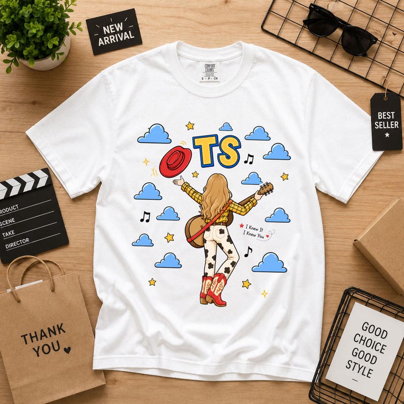 May include: A white short-sleeve t-shirt featuring a graphic of a blonde person with a guitar, a red cowboy hat, and cow-print pants. The design includes blue clouds, yellow stars, musical notes, the text TS, and the phrase I Knew It I Knew You.