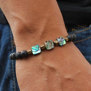 Puede incluir: Un brazalete de roca de lava negra con acentos cuadrados de concha de abulón y separadores de latón.