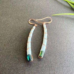 Könnte beinhalten: Ein Paar lange, weiße, muschelförmige Ohrringe mit Kupferdraht umwickelt. Jeder Ohrring hat eine grüne und blaue Abalone-Muschel am unteren Ende.