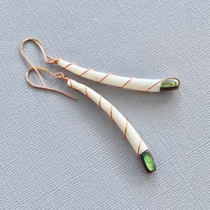 May include: A pair of long, curved earrings with a white shell and a green iridescent accent. The earrings are made with copper wire and have a simple, elegant design.