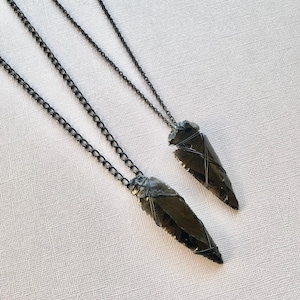 May include: Two black obsidian arrowhead pendants on black chain necklaces. The arrowheads are wrapped with black wire.