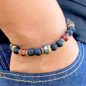 May include: A black lava rock bracelet with gold and silver beads, including a red and gold bead.