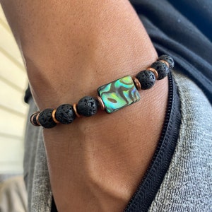 May include: A black lava rock bracelet with a copper spacer and a green abalone shell accent.