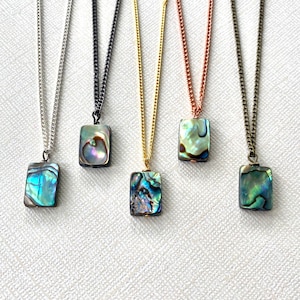 Pode incluir: Cinco colares com correntes de diferentes cores e pingentes de concha de abalone. Os pingentes são todos retangulares e têm uma cor azul e verde iridescente.