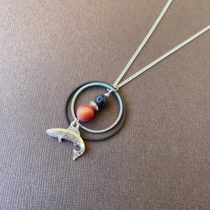 May include: Silver necklace with a fish charm, two silver rings, a red agate bead, and a black lava bead.