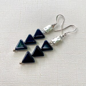 May include: A pair of dangle earrings featuring dark blue triangular beads. The earrings have silver-tone metal accents and ear wires. The triangular beads are arranged in a cascading design, creating a modern and geometric look.