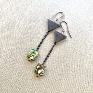 Könnte beinhalten: Ein Paar lange Ohrringe mit silberner Kette, an denen jeweils ein grauer Dreiecksanhänger und ein quadratischer Abalone-Muschel-Anhänger hängen.