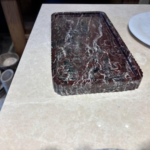 May include: A rectangular tray crafted from deep red marble with prominent white and black veining. The tray features a flat, recessed surface and a thick, vertically fluted edge that runs along the entire perimeter of the piece.