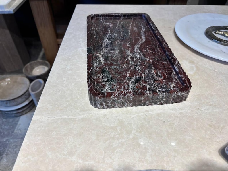 May include: A rectangular tray crafted from deep red marble with prominent white and black veining. The tray features a flat, recessed surface and a thick, vertically fluted edge that runs along the entire perimeter of the piece.