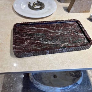 May include: A rectangular tray crafted from deep red marble with prominent white and dark grey veining. The tray features a distinctively fluted or ribbed edge design that runs along the entire perimeter, providing a textured border to the smooth surface.